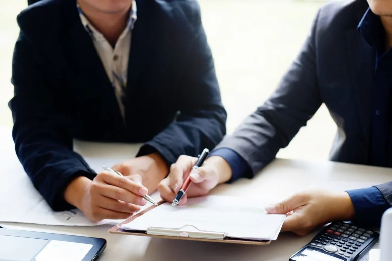 二人がペンを持ち一つの紙に何かを書こうとしている写真