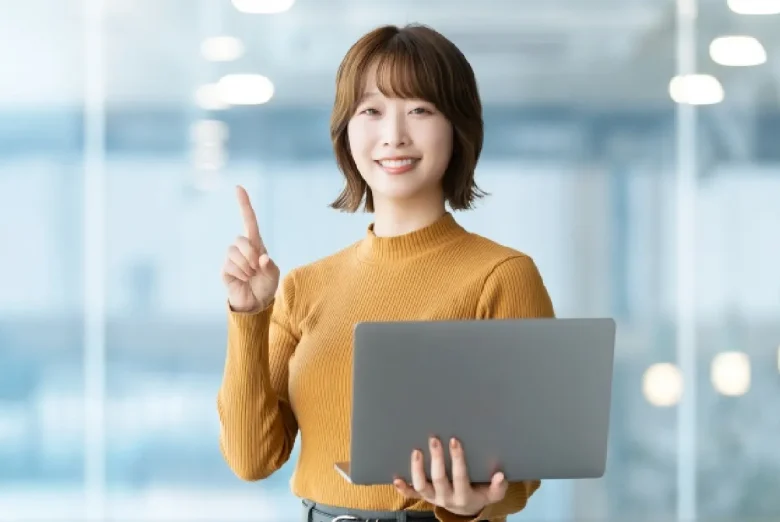 女性がパソコンを持ち右手の人差し指を立てている写真